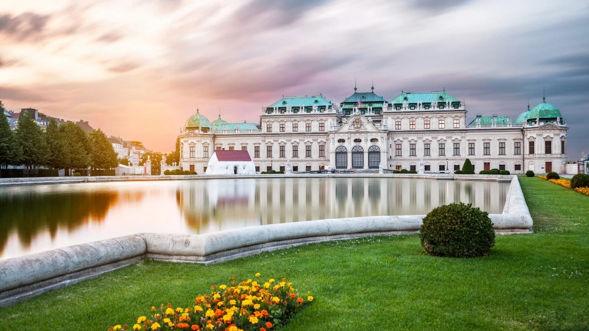 Belvedere Palace in Vienna during sunset, with a calm reflecting pool and vibrant flowers along the edge of the garden.