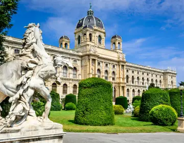 Kunsthistorisches Museum with a dome and statues in front, surrounded by manicured hedges.