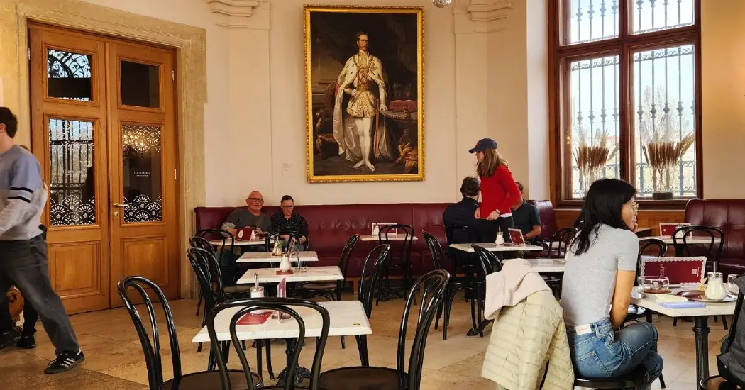Interior of Belvedere Palace café with black chairs and marble tables, showing visitors seated and enjoying the space.
