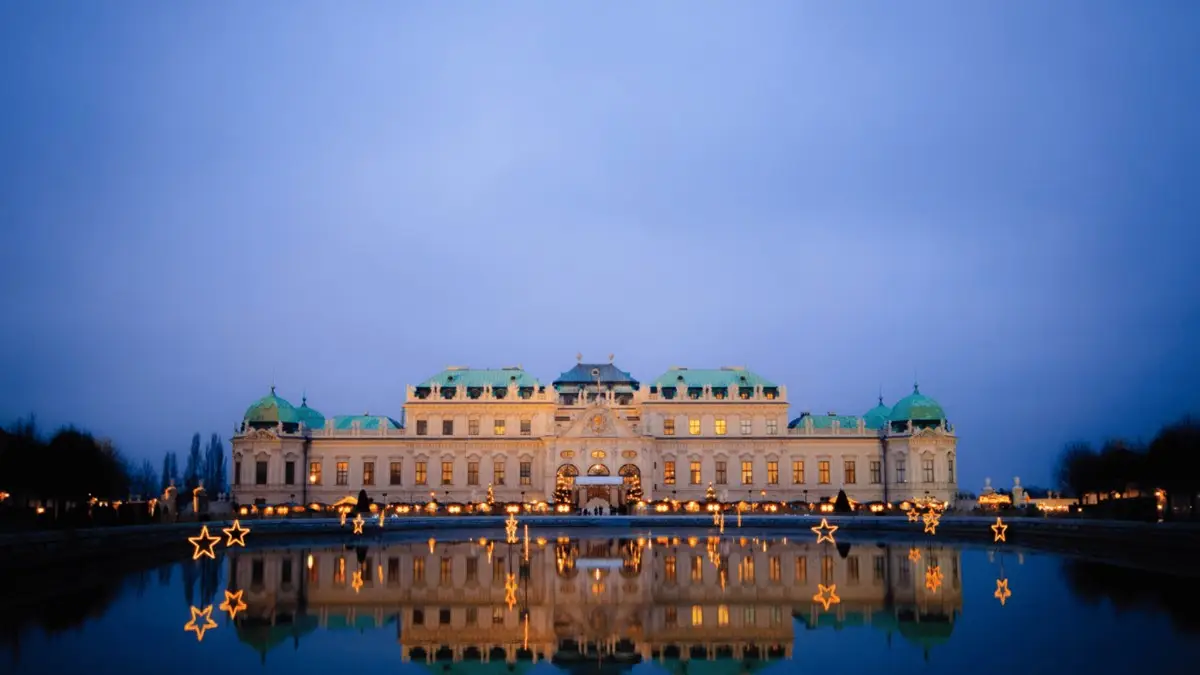 A view of Belvedere Palace at dusk, beautifully lit with Christmas lights and glowing star decorations reflecting in the water. A view of Belvedere Palace at dusk, beautifully lit with Christmas lights and glowing star decorations reflecting in the water.