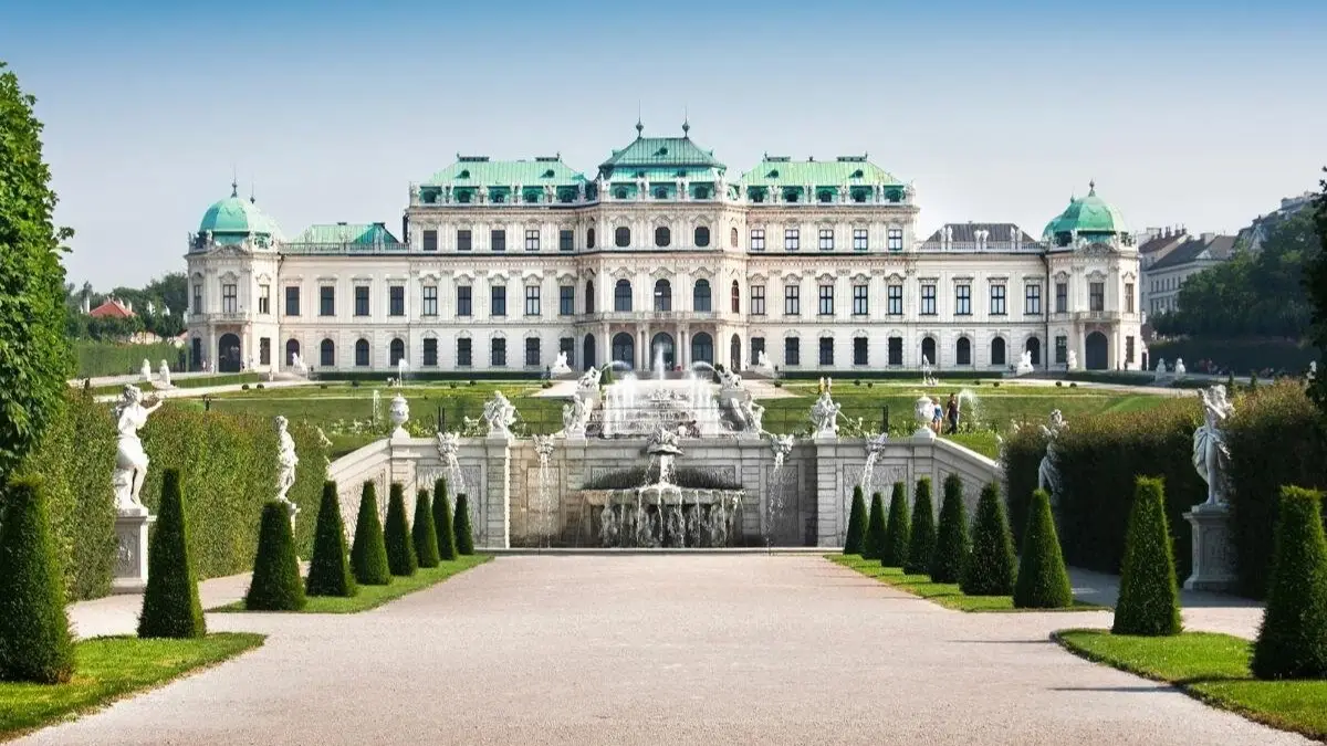Front view of Belvedere Palace with manicured gardens, statues, and a cascading fountain under a clear blue sky. Front view of Belvedere Palace with manicured gardens, statues, and a cascading fountain under a clear blue sky.