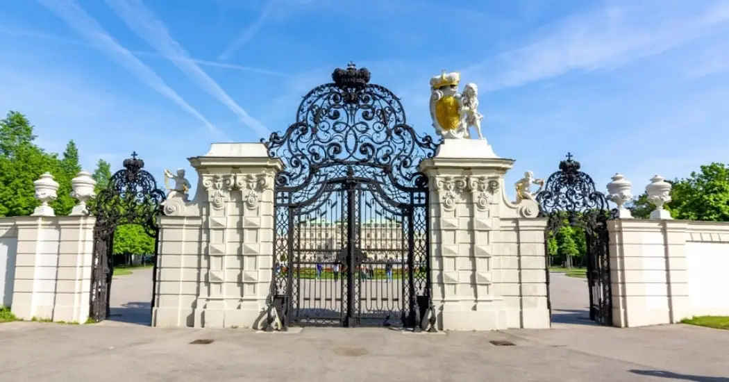 Ornate black iron gate at the main entrance of Belvedere Palace with clear blue sky.