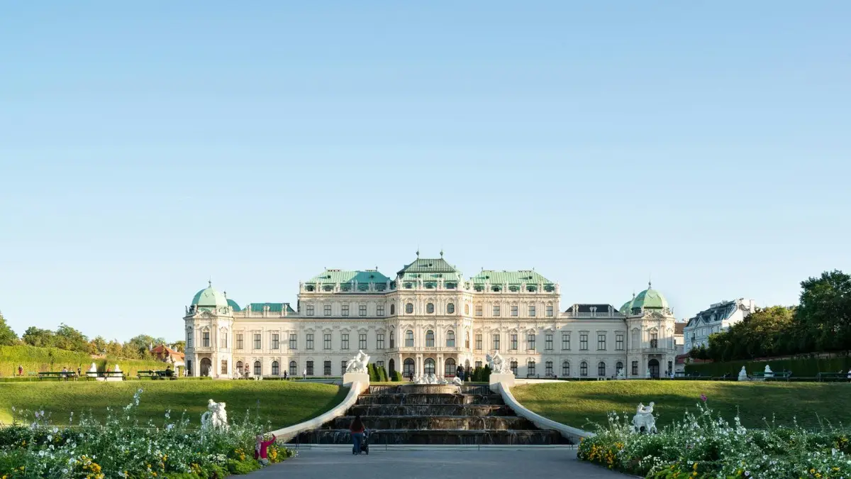 The Belvedere Palace in Vienna, seen from the garden with a cascading fountain and colorful flowers in front. The Belvedere Palace in Vienna, seen from the garden with a cascading fountain and colorful flowers in front.