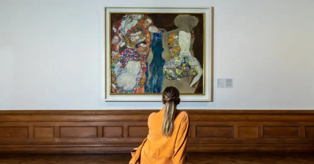 A woman is admiring the colorful painting by Gustav Klimt in the Belvedere Museum.
