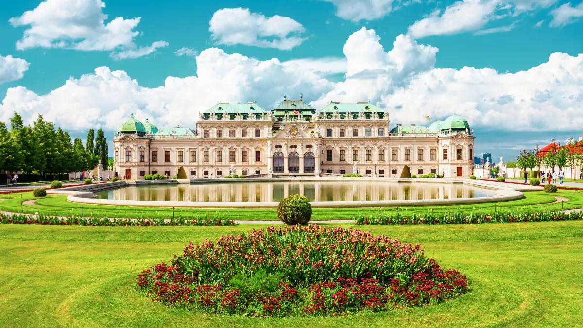 The Belvedere Palace with a beautiful garden and a large reflecting pool under a bright blue sky.