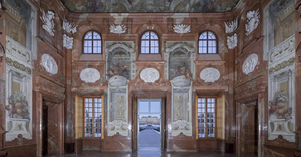 Interior view of the Lower Belvedere Palace in Vienna, showing a hall with marble walls and detailed frescoes.