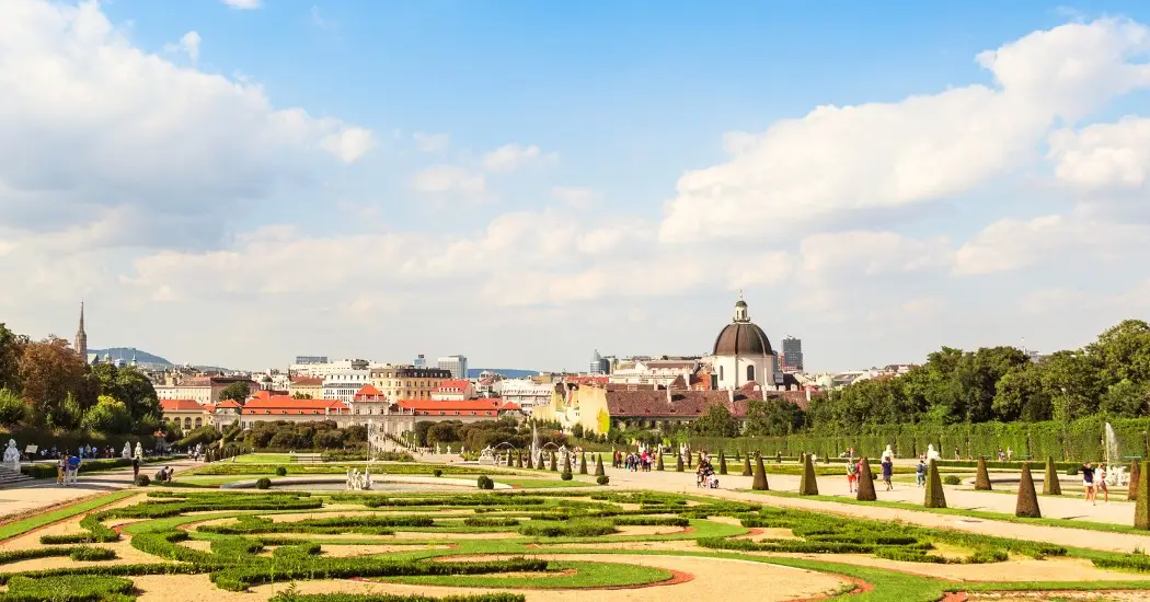 Tourists walking in the Belvedere Gardens with trimmed hedges and city views.