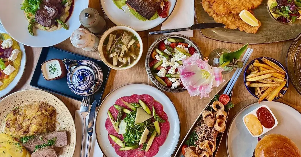 Various dishes served on plates, including steak, fish, salad, fries, soup, and a burger on a wooden table.