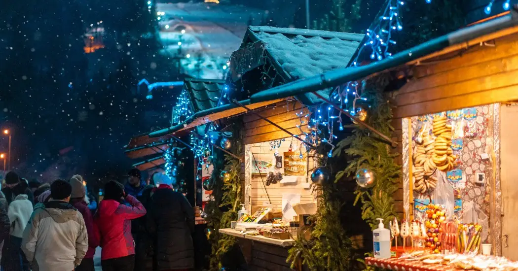 People browsing wooden Christmas stalls under fairy lights at night