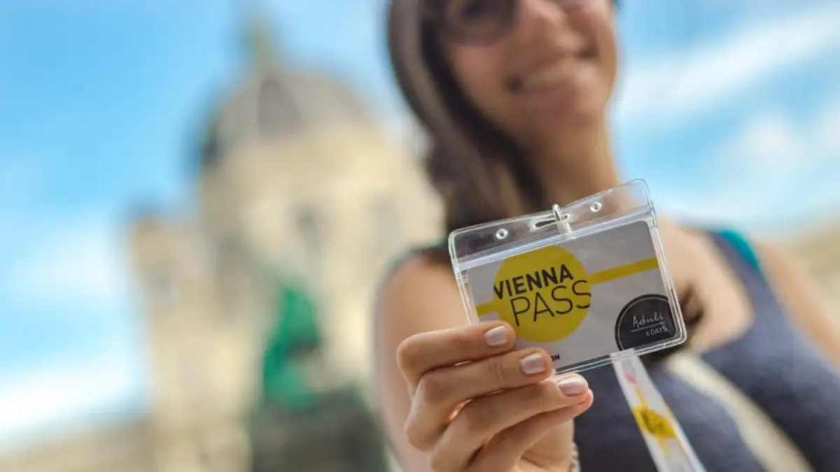 A smiling tourist is holding up a Vienna PASS card.