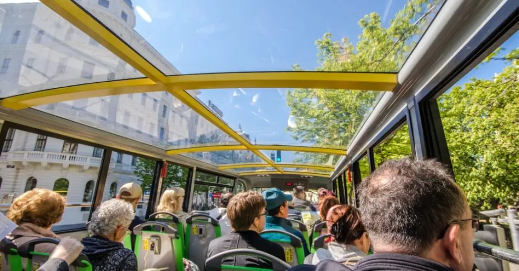 Passengers enjoy a sunny city tour on a glass-roof hop-on hop-off bus in Vienna.